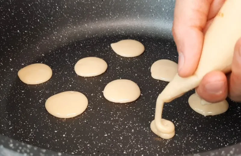 Процесс обжарки панкейков на сковороде с характерными пузырьками на поверхности.