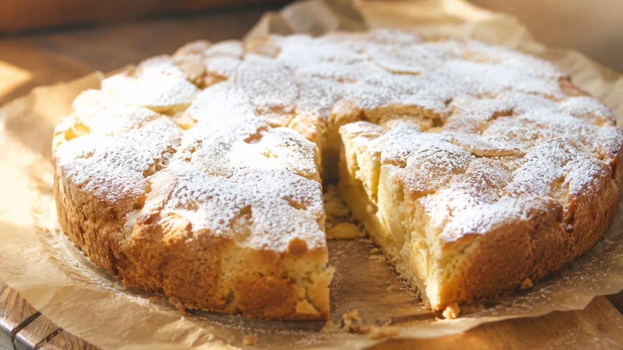 Готовая шарлотка с яблоками на круглом блюде с золотистой корочкой